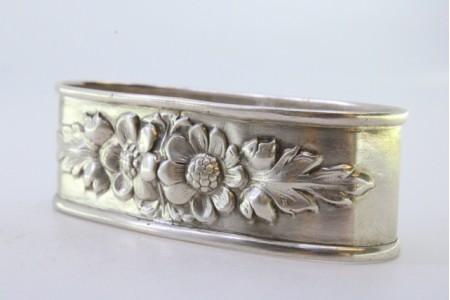 Argola de guardanapo em prata de forma oval com flores relevadas.
